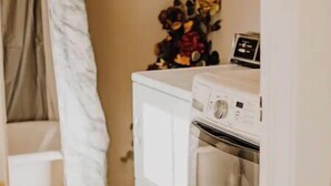 A compact laundry room with a washing machine and dryer, a small white cabinet, and a curtain.