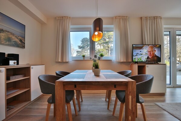 A modern dining area with a wooden table, grey chairs, a hanging pendant light, and a television on a stand. - Villa Stern Appartement 2 (Timmendorfer Strand)