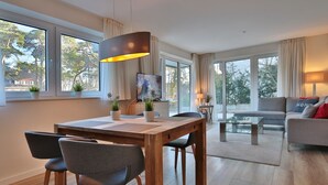 A modern living room with a wooden dining table, grey chairs, a sofa, and a TV. - Villa Stern Appartement 2 (Timmendorfer Strand)