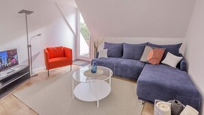 Un salon moderne avec un canapé, une table basse en verre, un fauteuil rouge et un téléviseur.