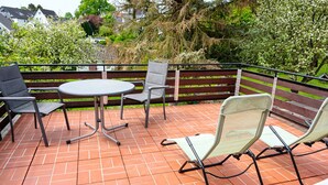 Une terrasse extérieure avec une table ronde et quatre chaises, entourée d’une clôture en bois et de verdure.