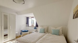 Une chambre à coucher avec un lit, une chaise, une armoire et une fenêtre avec des rideaux.