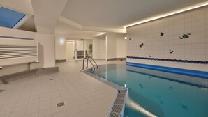 Ein Schwimmbecken mit einer Fliesenwand, einer Metallleiter und einer Decke mit einem Oberlicht.