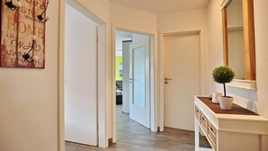 Ein Flur mit einer zurueckfuehrenden Tür, einem kleinen Blumentopf auf einer Konsole und einer Wanddekoration.