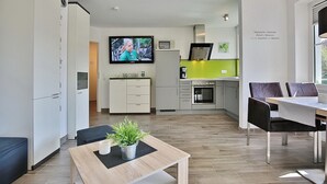 Eine moderne Küche mit Fernseher, ein Essbereich mit Tisch und Stühlen und eine kleine Sitzecke mit einer Couch.