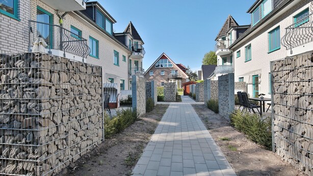 Eine Wohnstraße mit Häusern auf beiden Seiten, einem gepflasterten Gehweg und einer Steinmauer.