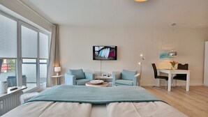 Une chambre d’hôtel moderne dotée d’un grand lit, d’un téléviseur fixé au mur, d’un coin repas avec une table et des chaises, et de grandes fenêtres offrant une vue panoramique.