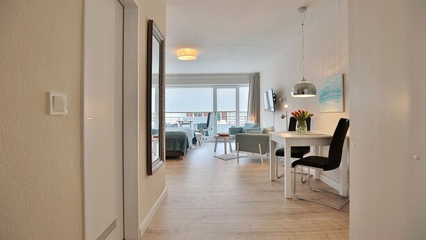 Une chambre d’hôtel moderne avec un plancher en bois, un coin repas comprenant une table et des chaises, et une grande fenêtre donnant sur la ville.