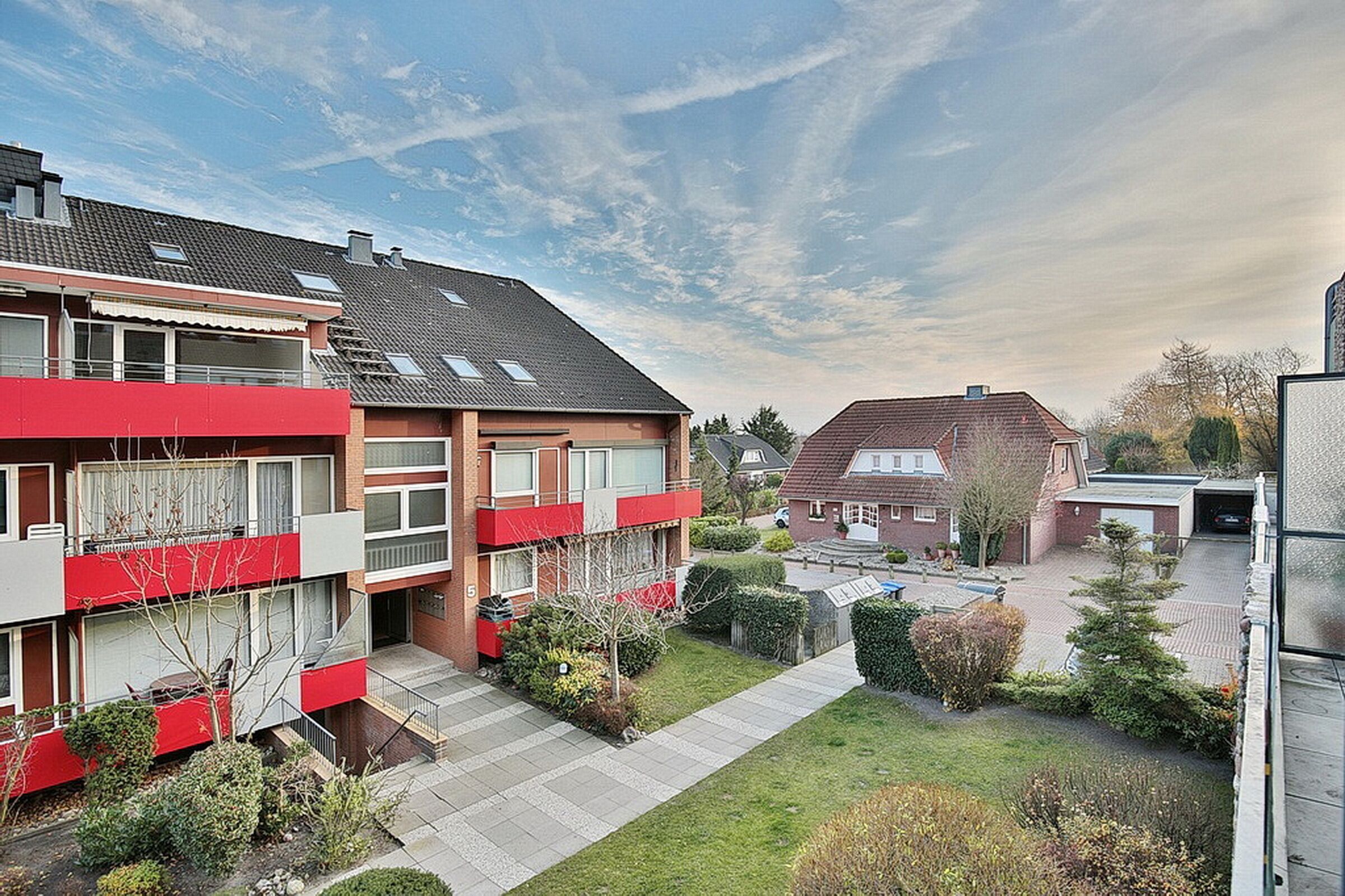 A residential building with multiple balconies, a paved courtyard, and surrounding greenery.