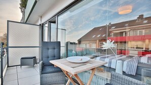 Un balcon doté de meubles en osier, d’une petite table et d’une paroi en verre.