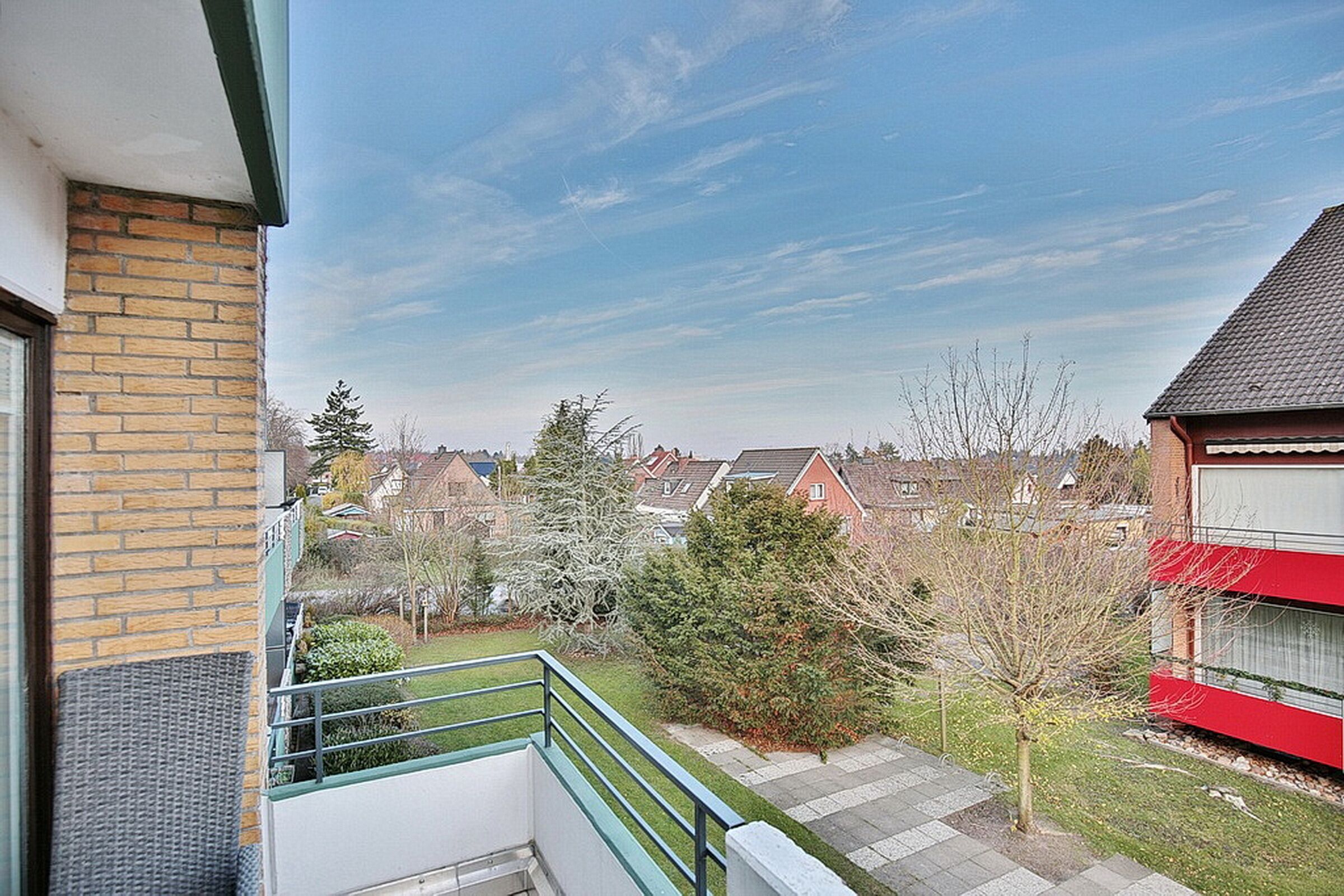 Un balcon d’habitation offrant une vue sur les maisons et les arbres des environs.