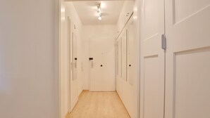 En smal hall med vita väggar och trägolv som leder fram till en dörr längst in.