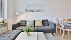 Ett modernt vardagsrum med en grå soffa, ett vitt soffbord och en tavla som föreställer en strandscen.