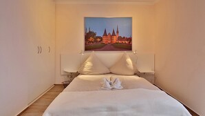 Ein Hotelzimmer mit einem großen Bett, einem Nachttisch, einer Wandleuchte und einem gerahmten Bild eines Schlosses.