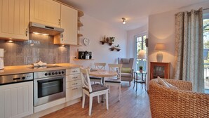 A modern kitchen with white cabinets, a built-in oven, and a dining area with a round table and chairs. - Villa am Meer Strandallee 48 Appartement 10 (Timmendorfer Strand)