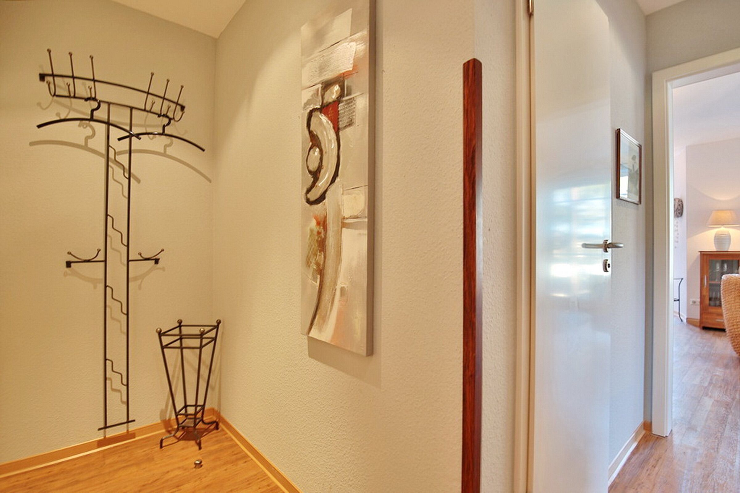 A hallway with a coat rack, a wall-mounted abstract art piece, and a wooden floor.