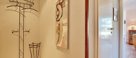 A hallway with a coat rack, a wall-mounted abstract art piece, and a wooden floor.