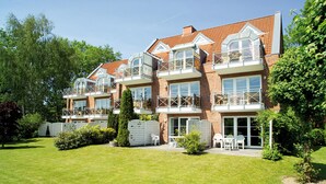 A multi-story residential building with balconies, a well-maintained lawn, and a brick facade.