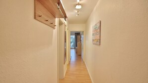 A narrow hallway with wooden flooring and white walls. There is a ceiling light fixture and a door at the end of the hallway.