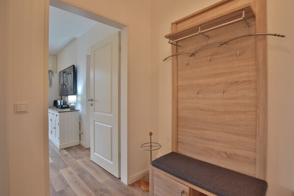 A hallway with a wooden bench, a coat rack, and a door leading to a kitchen area. - Wohnpark Niendorf 13 Appartement 4 (Niendorf/Ostsee)