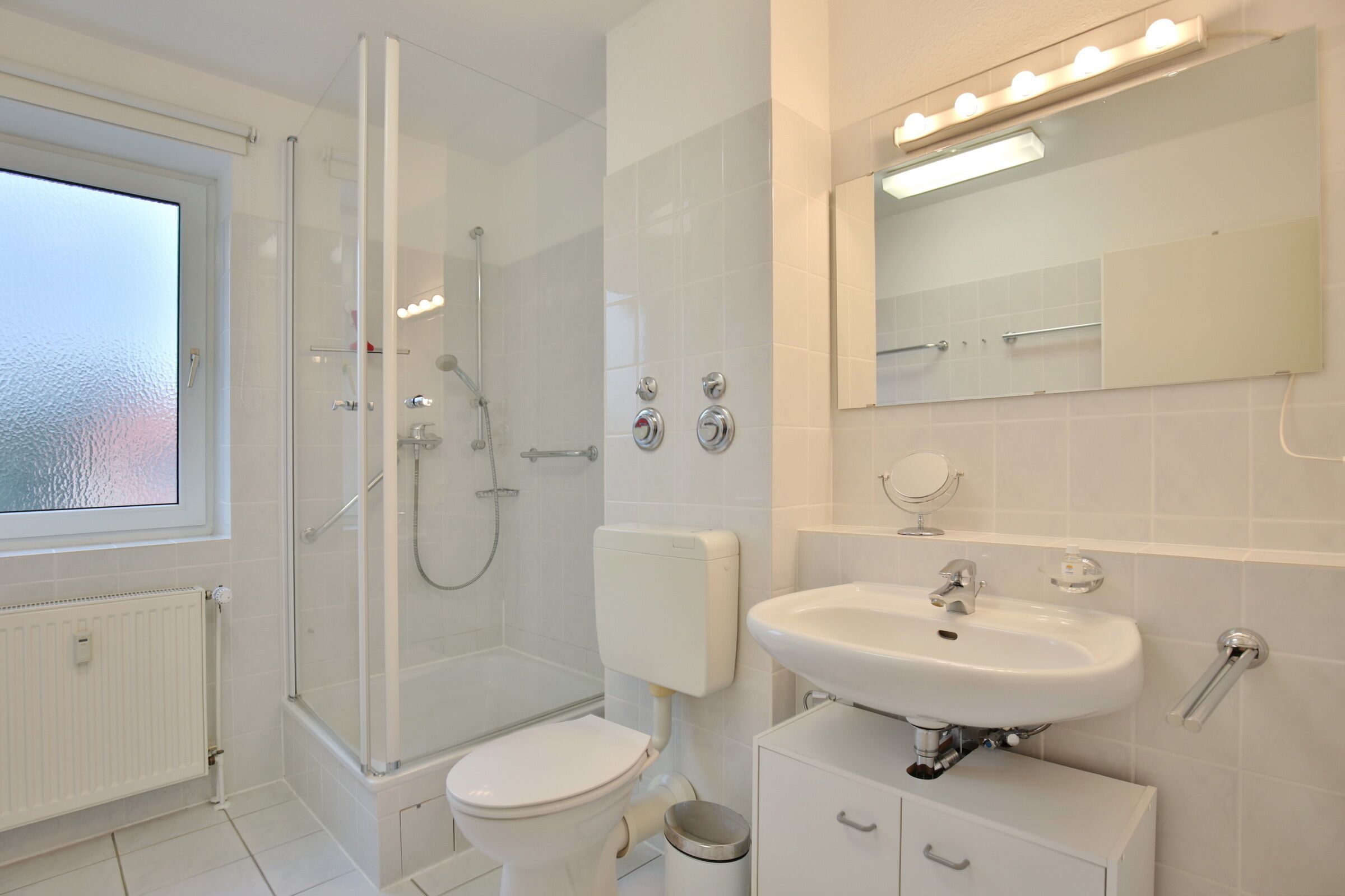 Een moderne badkamer met een douchecabine van glas, een toilet, een wastafel en een spiegel.