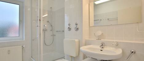 Een moderne badkamer met een douchecabine van glas, een toilet, een wastafel en een spiegel.