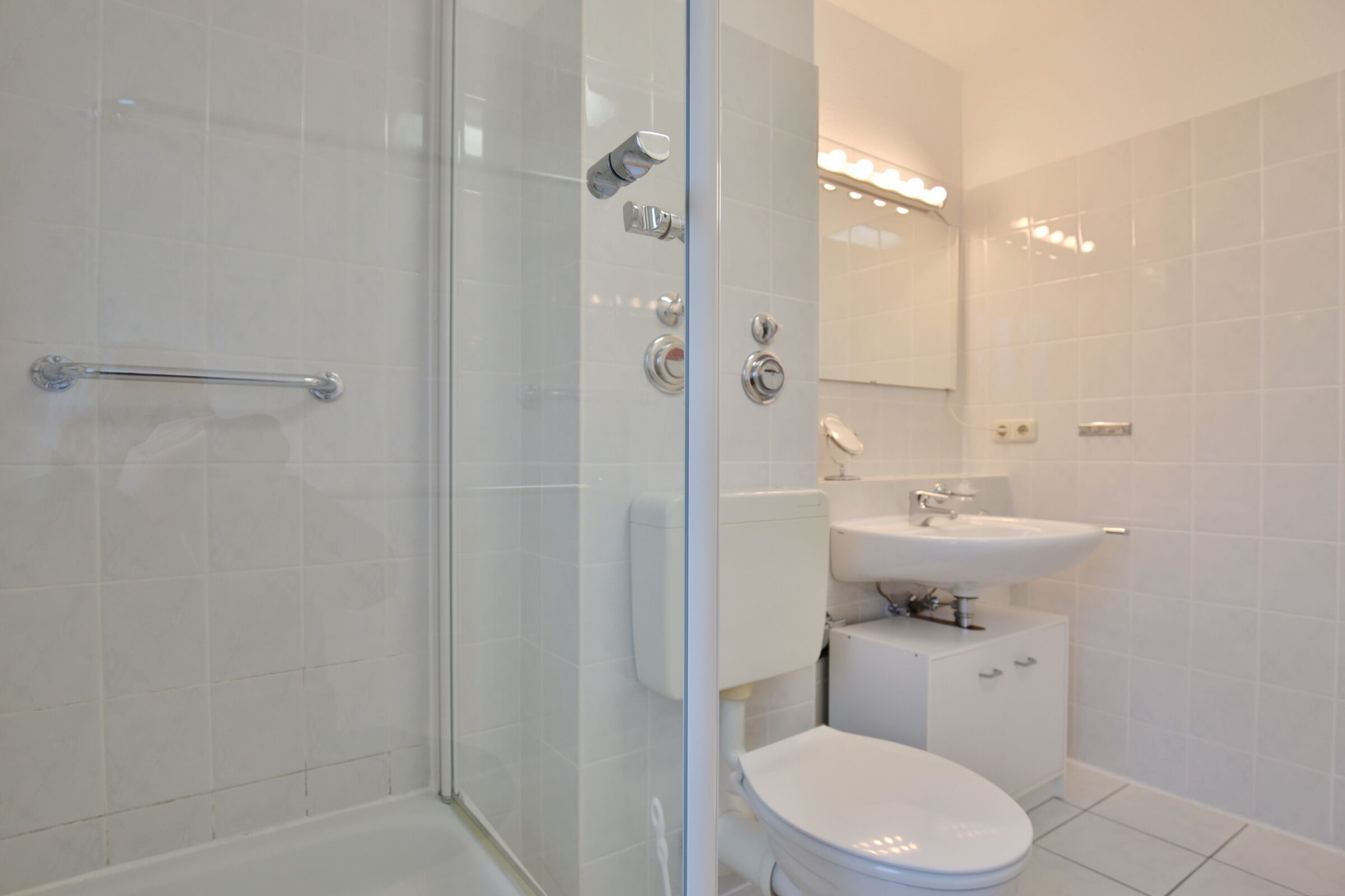 Un baño moderno con cabina de ducha de vidrio, inodoro blanco y lavabo con espejo.