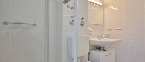 Un baño moderno con cabina de ducha de vidrio, inodoro blanco y lavabo con espejo.