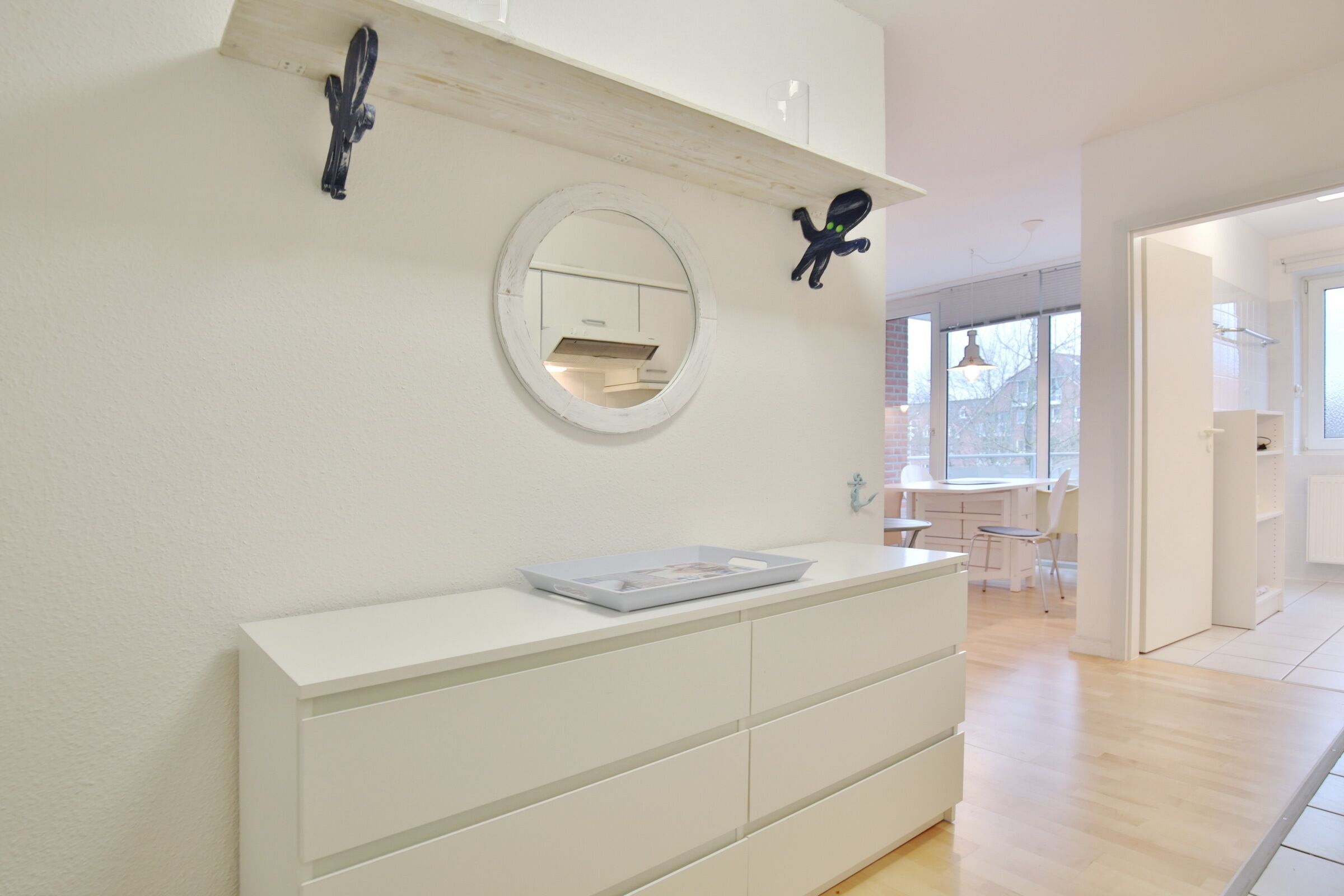 A modern, minimalist room with a white dresser, a round mirror, and two wall-mounted octopus decorations.