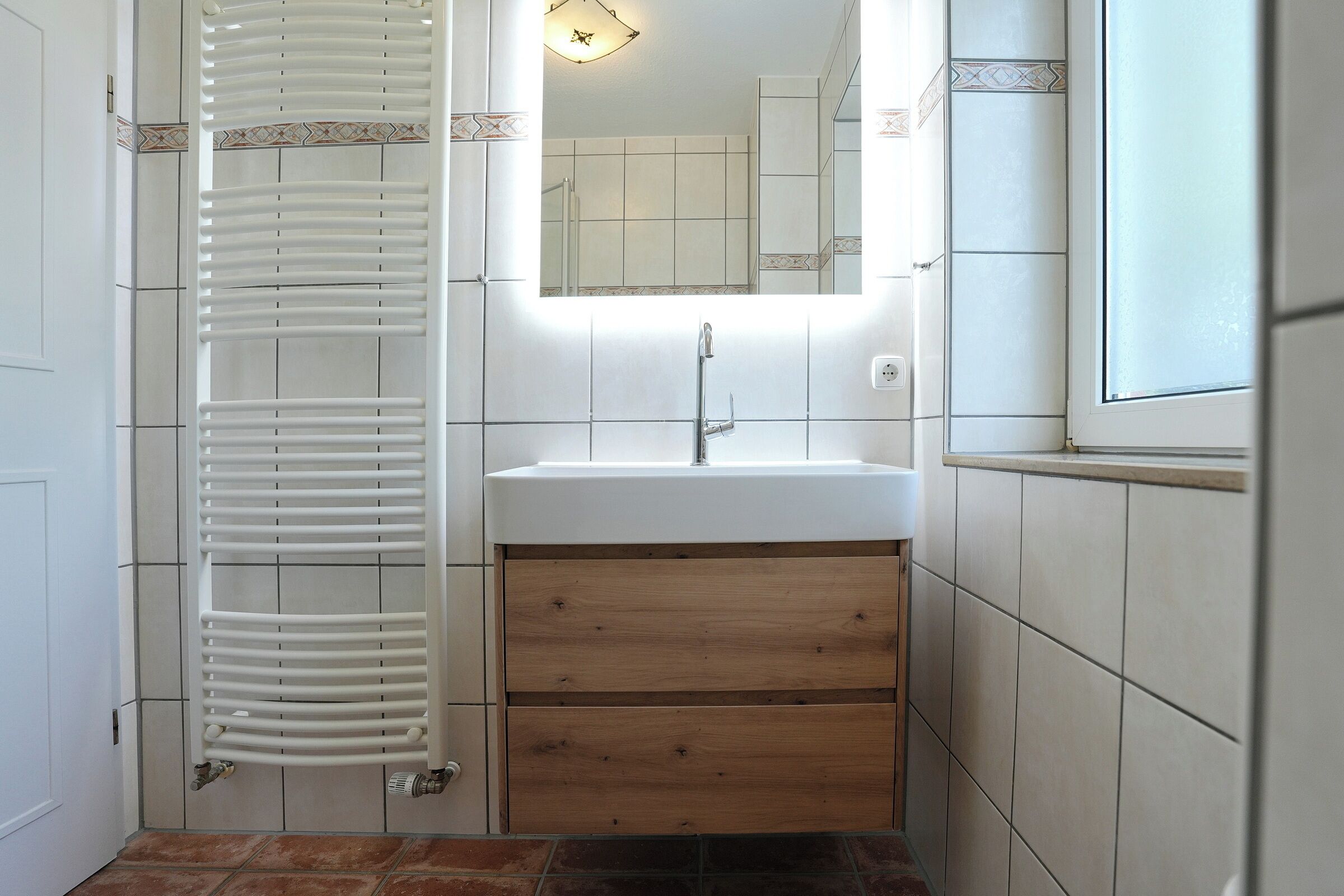 Een badkamer met een witte wastafel, een houten kast en een handdoekhouder.