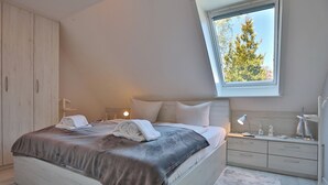 A bedroom with a bed, bedside tables, a wardrobe, and a window with a view of trees. - Am Elchgrund Appartement 10 (Timmendorfer Strand)
