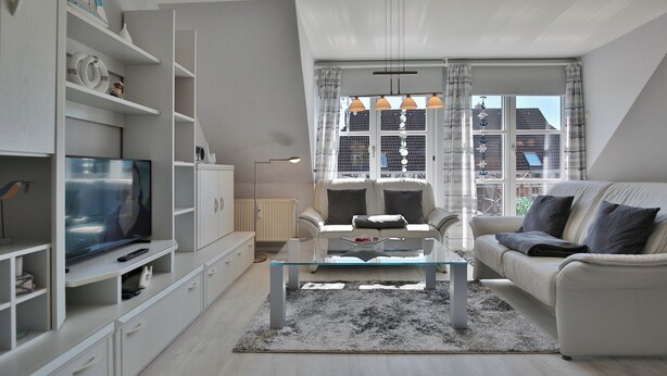 A modern living room with a glass coffee table, white sofa, and a television on a white cabinet. - Am Elchgrund Appartement 10 (Timmendorfer Strand)