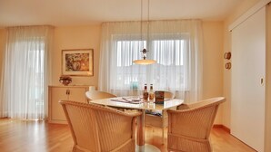 Un coin repas avec une table ronde, des chaises en osier, un luminaire suspendu et un tableau au mur.