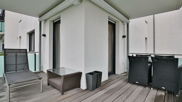 Un espace extérieur abrité comprenant une table en verre, une chaise en osier et deux chaises noires.
