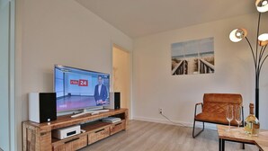 Un salon moderne avec un meuble de rangement en bois pour l’équipement audiovisuel, un téléviseur à écran plat, un fauteuil en cuir marron et une table avec des verres et une bouteille.