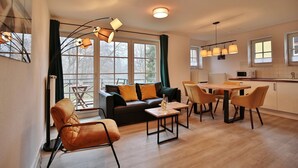 Un salon moderne comprenant un canapé, une table basse et des fauteuils, un coin repas avec une table et des chaises, et une cuisine équipée d’un four à micro-ondes et d’une cuisinière.