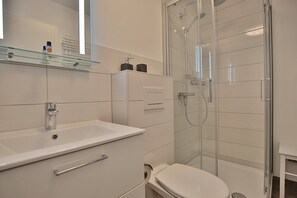Ein modernes Badezimmer mit einer Duschkabine aus Glas, einem weißen Waschbecken mit Spiegel und einer Toilette.