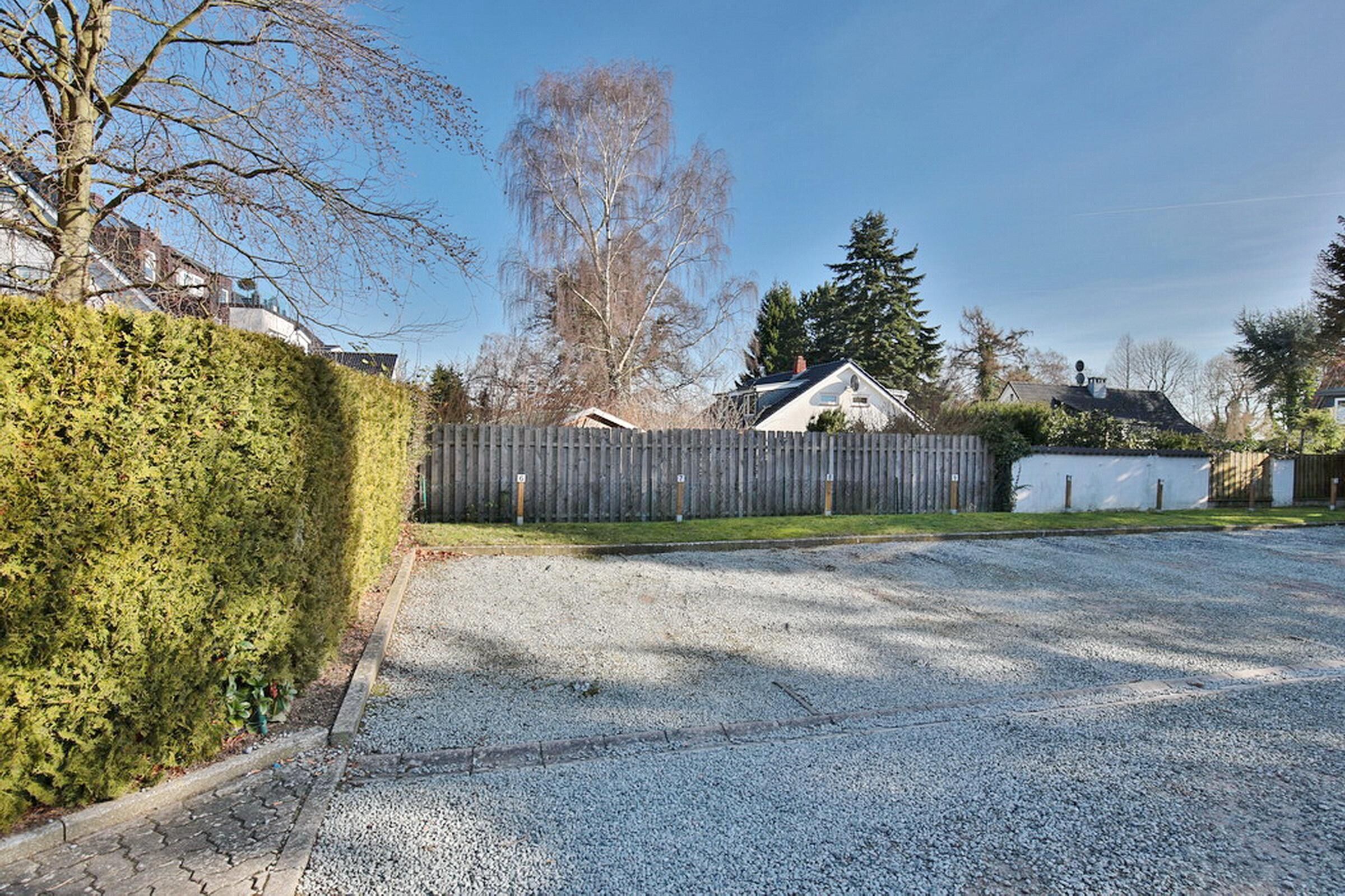 A residential driveway with a gravel surface, a wooden fence, and a house in the background.