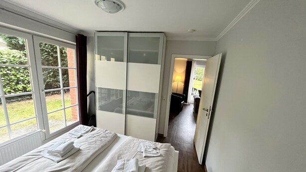 A bedroom with a large bed, a wardrobe, and a view of the garden. - Haus Parkblick Appartement 3 (Timmendorfer Strand)