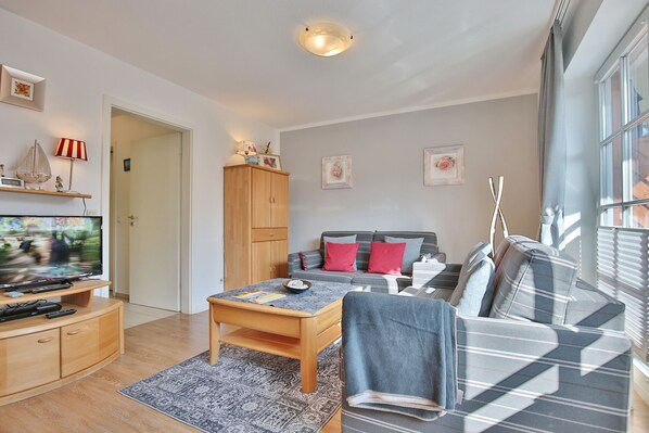 A modern living room with a sofa, coffee table, and TV. There is a wooden cabinet and a door leading to another room.