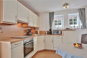 A modern kitchen with white cabinets, a microwave, and a coffee maker. There is a dining table with a fruit bowl.
