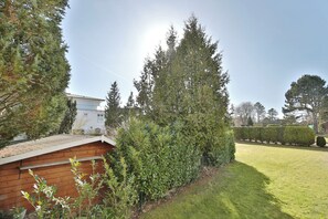 A well-maintained garden with a wooden structure, neatly trimmed hedges, and a clear sky.