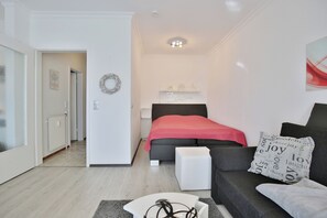 A modern bedroom with a bed, a grey sofa, a white side table, and a grey rug.