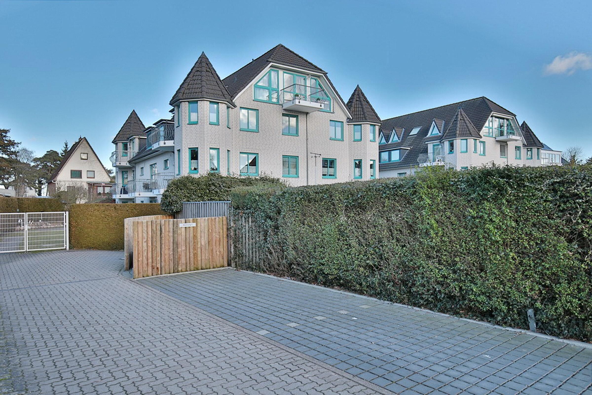A modern residential building with multiple levels, a gated entrance, and a paved driveway.