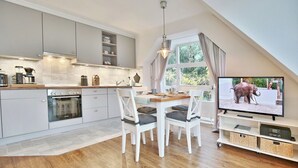 Eine moderne Küche mit weißen Schränken, einem Einbauofen und einem Essbereich mit weißen Stühlen und einem Holztisch.