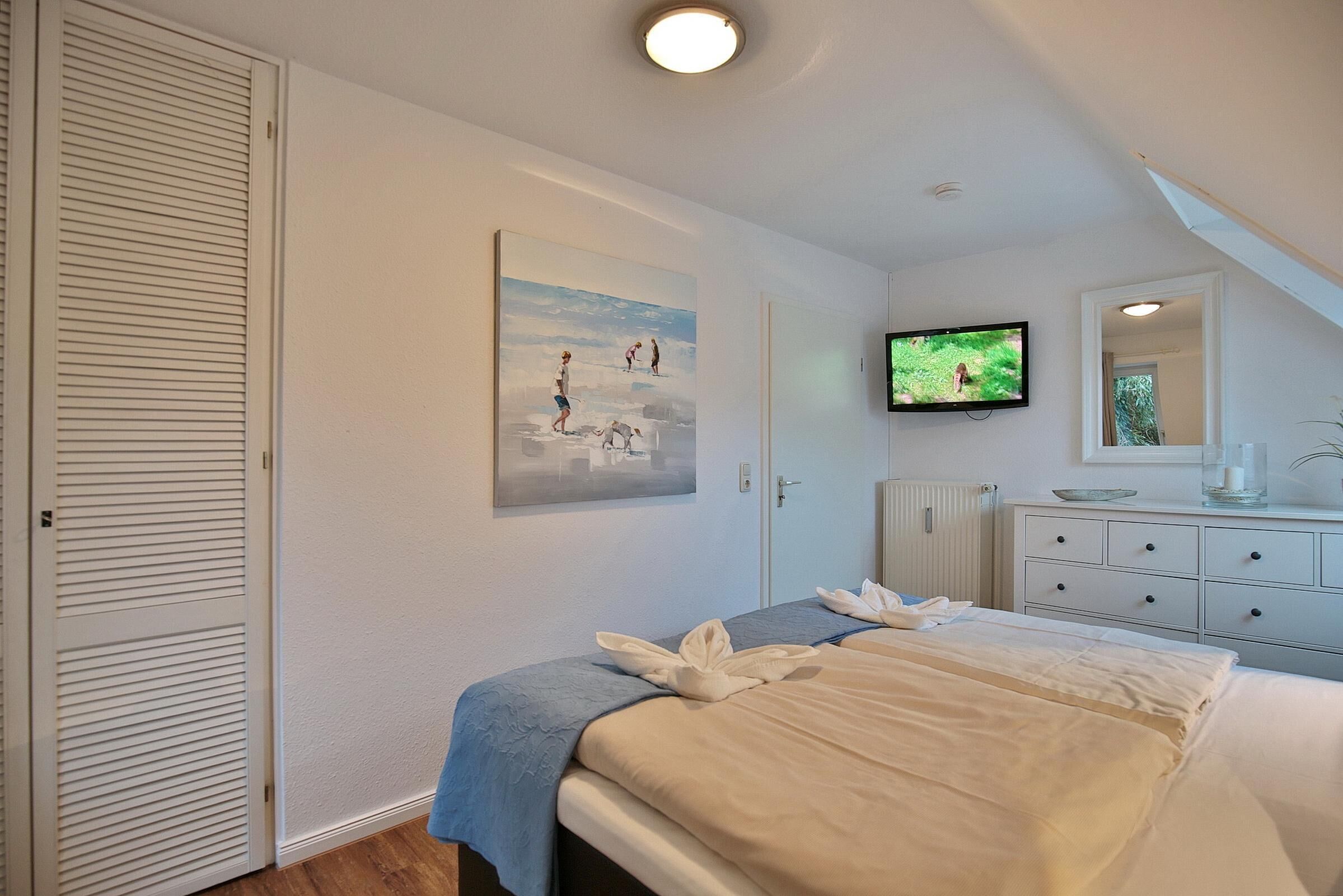 Quarto de hotel com cama, televisão, quadro e cômoda.
