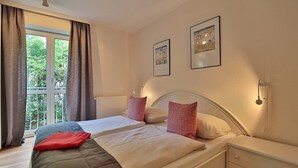 Un dormitorio con cama, mesitas de noche, una ventana con cortinas e imágenes colgadas en la pared.