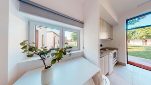 A modern kitchen with white cabinetry, a countertop, and a window overlooking a garden.