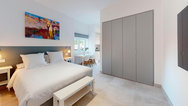 A modern bedroom with a large bed, bedside tables, a desk, and a wardrobe.