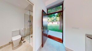 A modern bathroom with a glass shower enclosure, a toilet, and a door leading to a courtyard. - One Bedroom Apartment (Toledo)